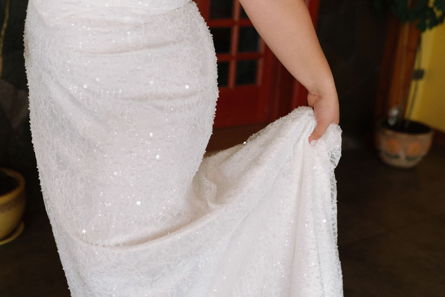 Close-up of a bride in a white sequined wedding gown holding up the train of her dress.