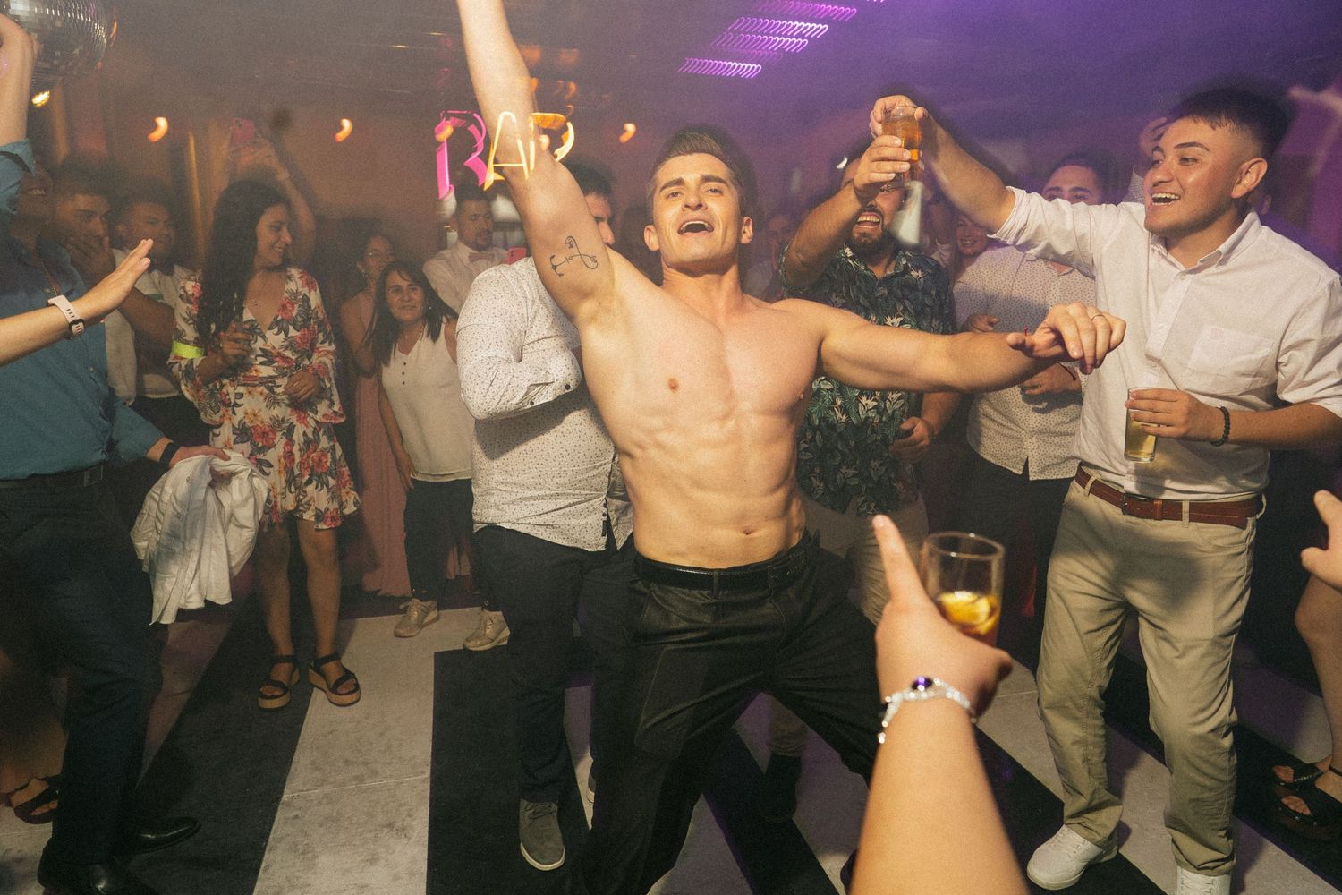 Shirtless guest dancing enthusiastically at a wedding reception with crowd cheering.