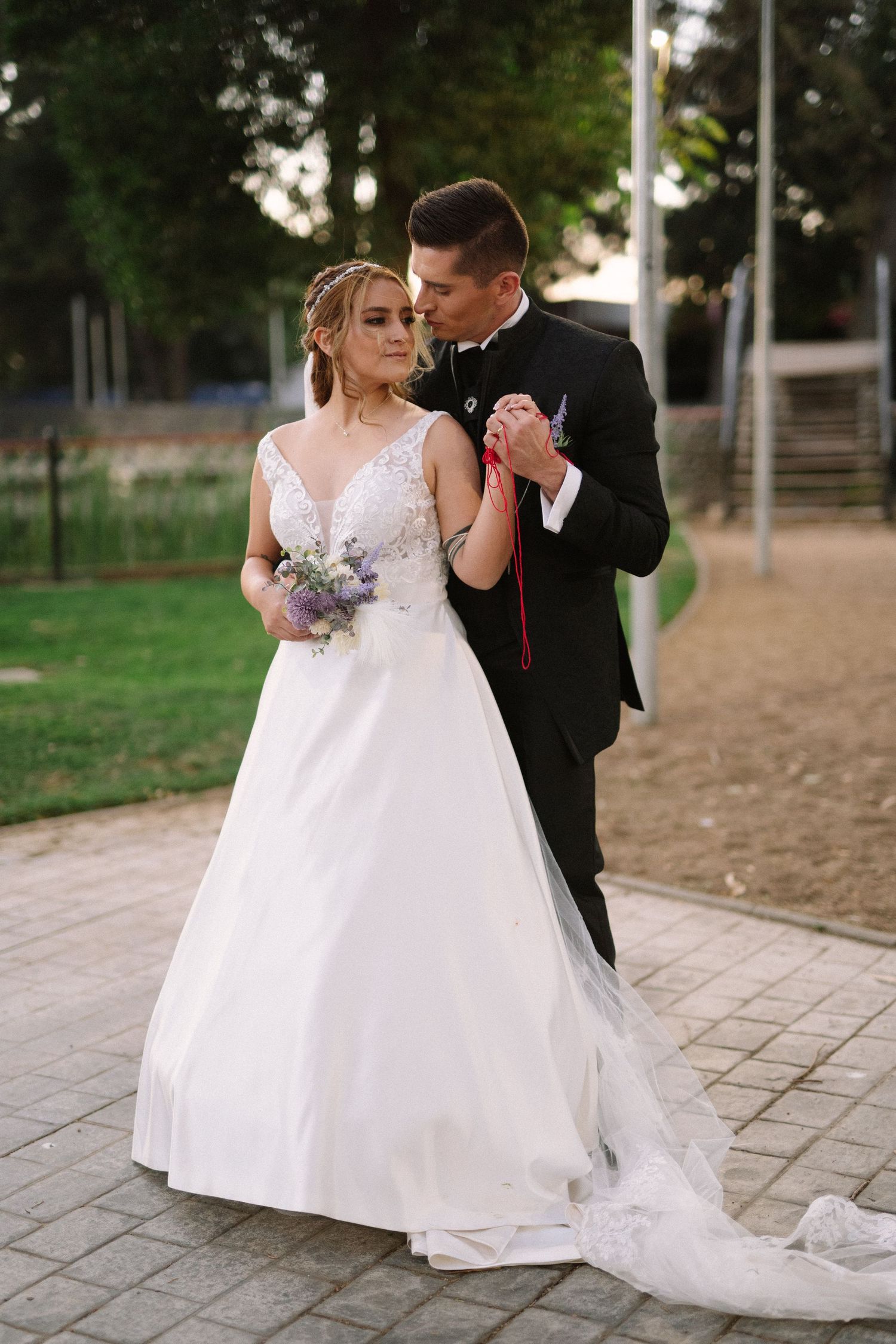 Elegant wedding couple shares an intimate dance moment while holding a purple bouquet outdoors.