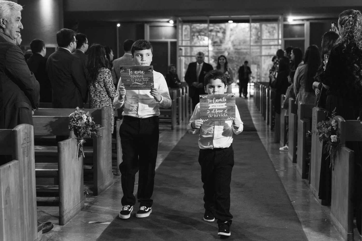 Two ring bearers walk down the church aisle at a wedding wearing matching outfits.