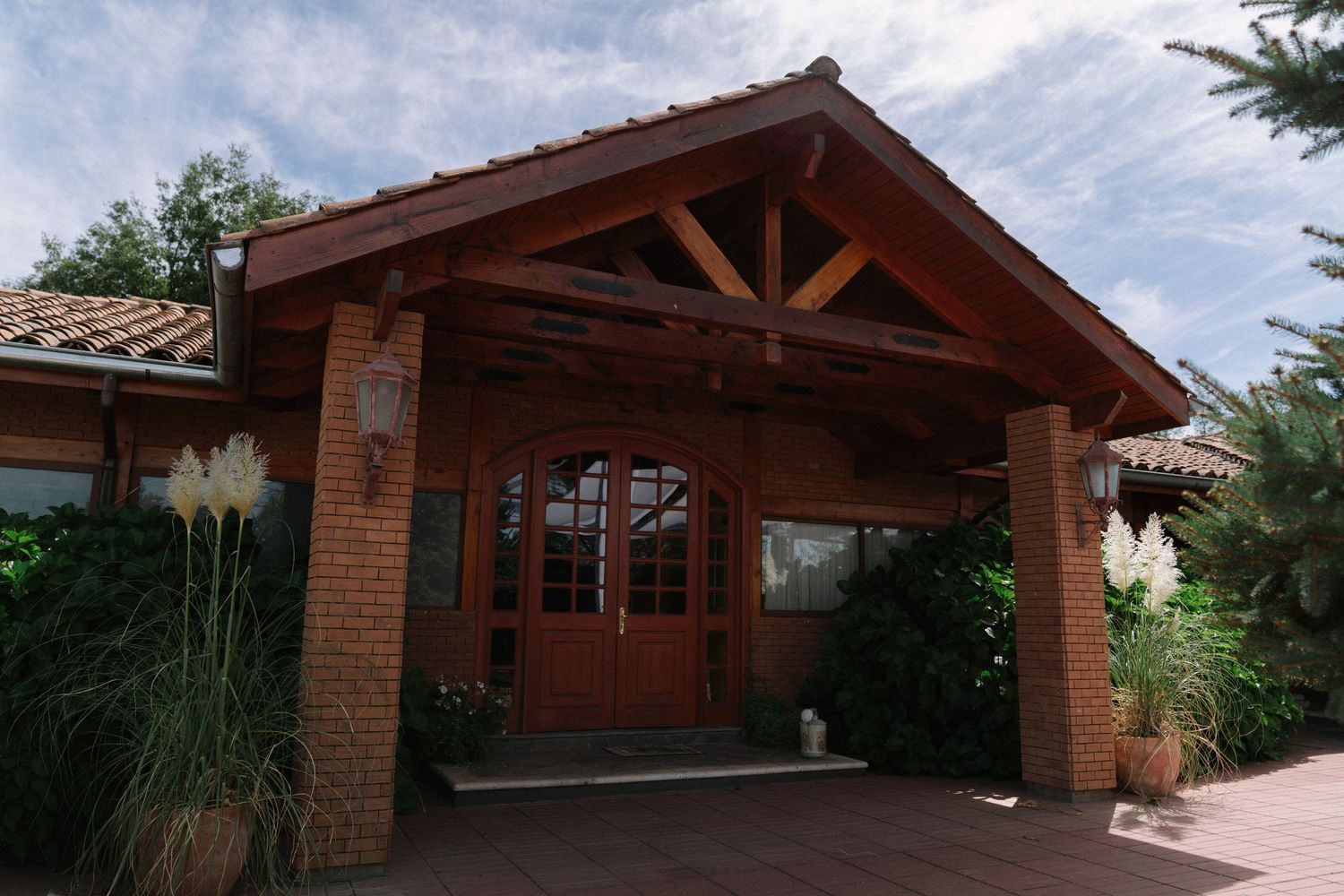 Rustic brick and wood wedding venue entrance with elegant double doors and lush greenery.
