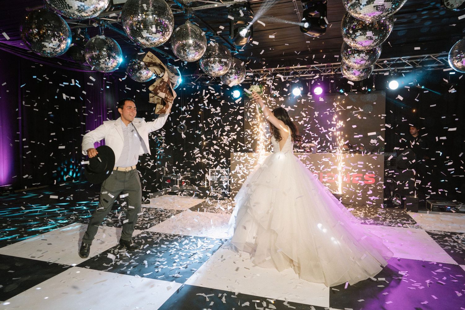 A spectacular wedding dance moment with confetti and disco lights on a black and white checkered floor.