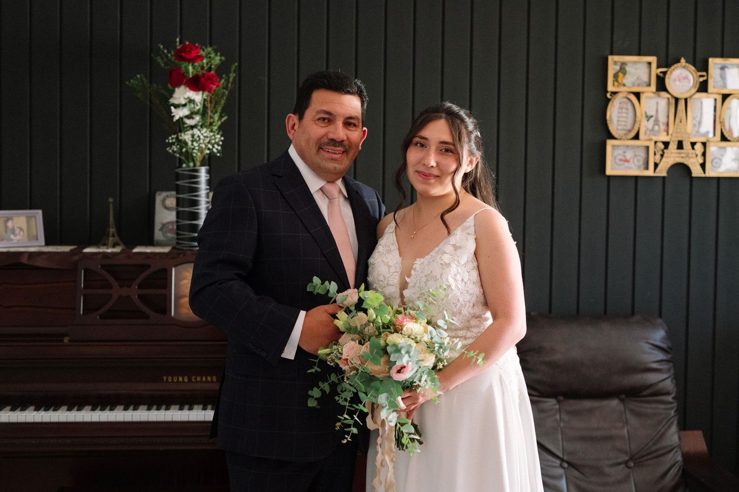 Newlyweds pose together in front of piano with bride holding floral bouquet.