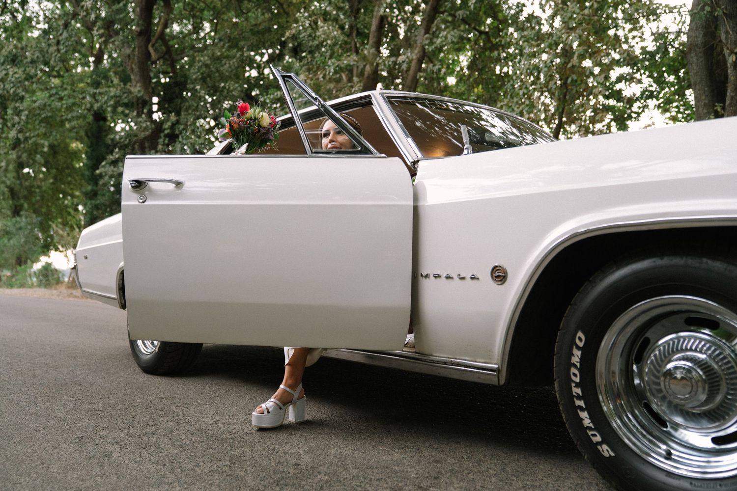 Classic white Cadillac convertible with chrome trim and fins parked on a tree-lined street.
