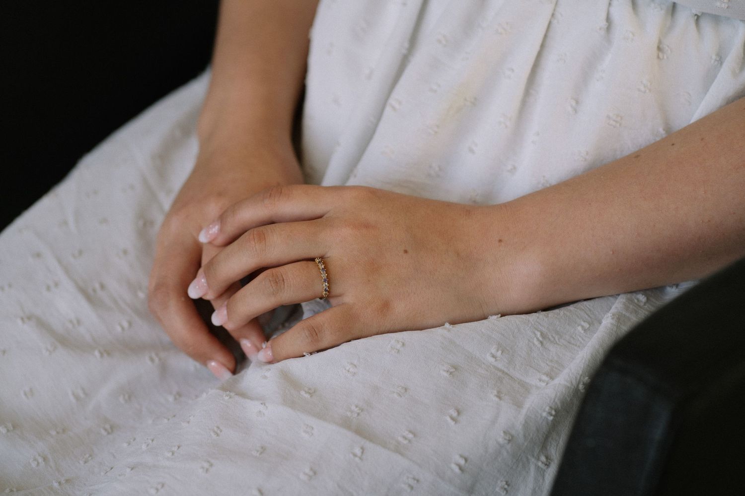 Close-up of hands with engagement ring resting on white eyelet fabric.