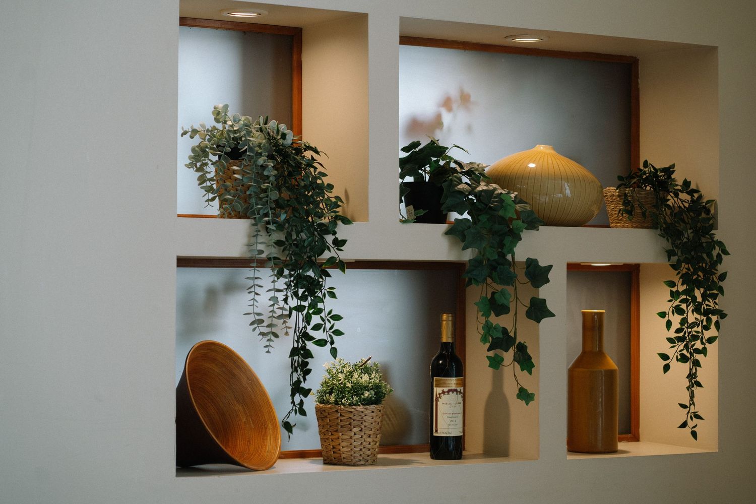 Built-in wall shelving with decorative wine bottles, wooden bowls, and trailing plants.