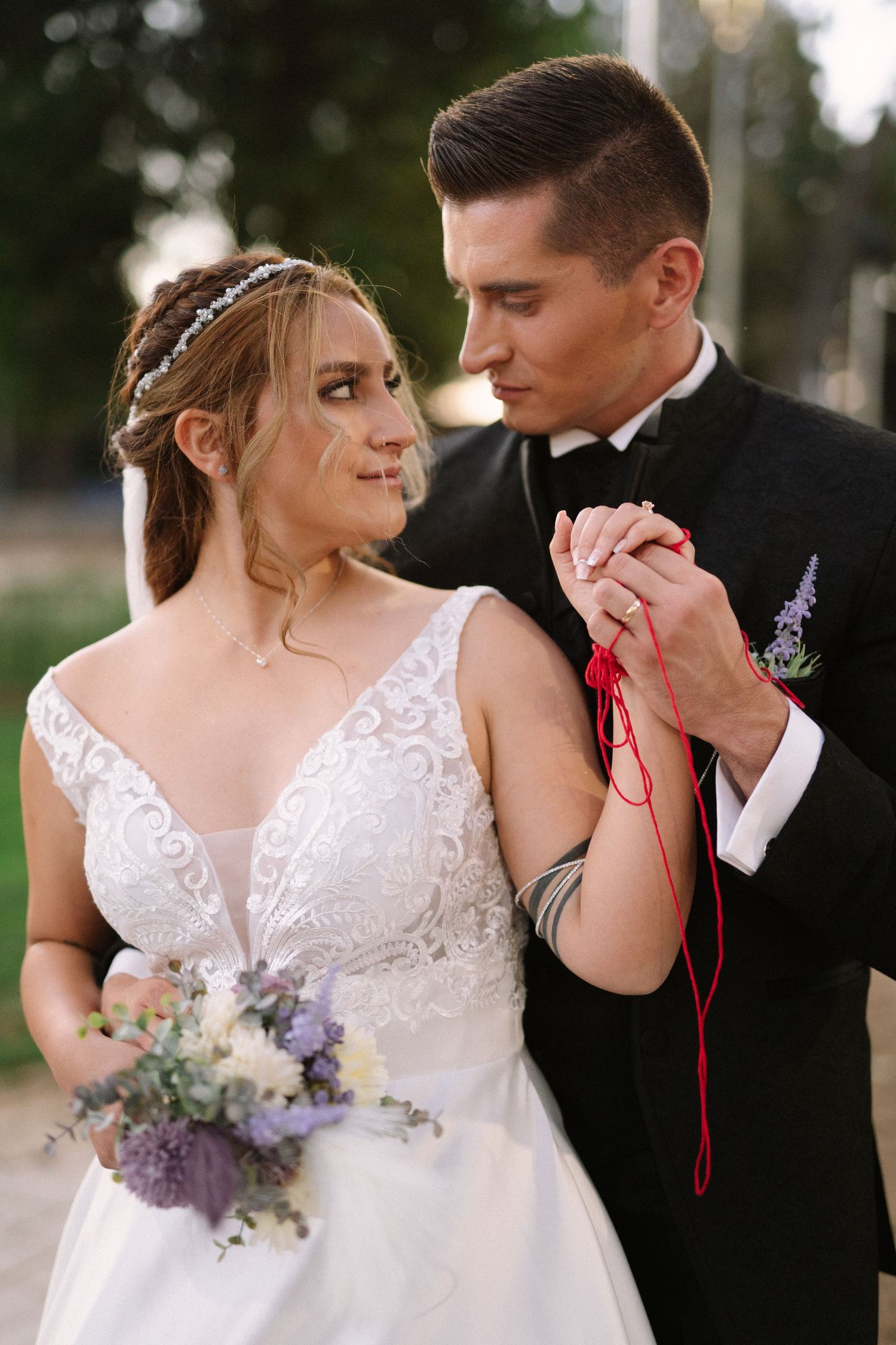 A wedding couple shares an intimate moment while holding hands with a red ribbon.