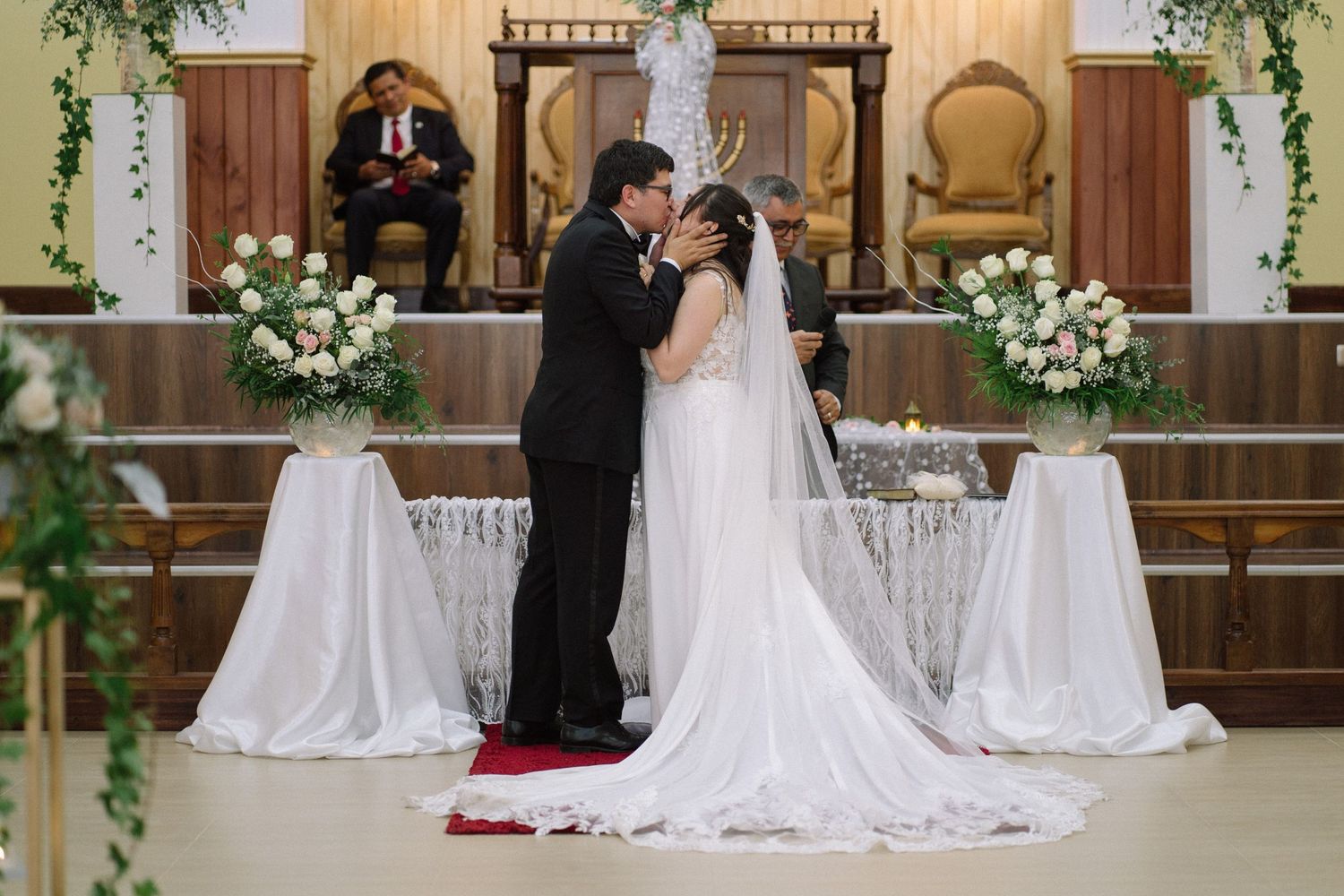 A wedding ceremony in a church with elegant white floral arrangements and draped fabric decorations.