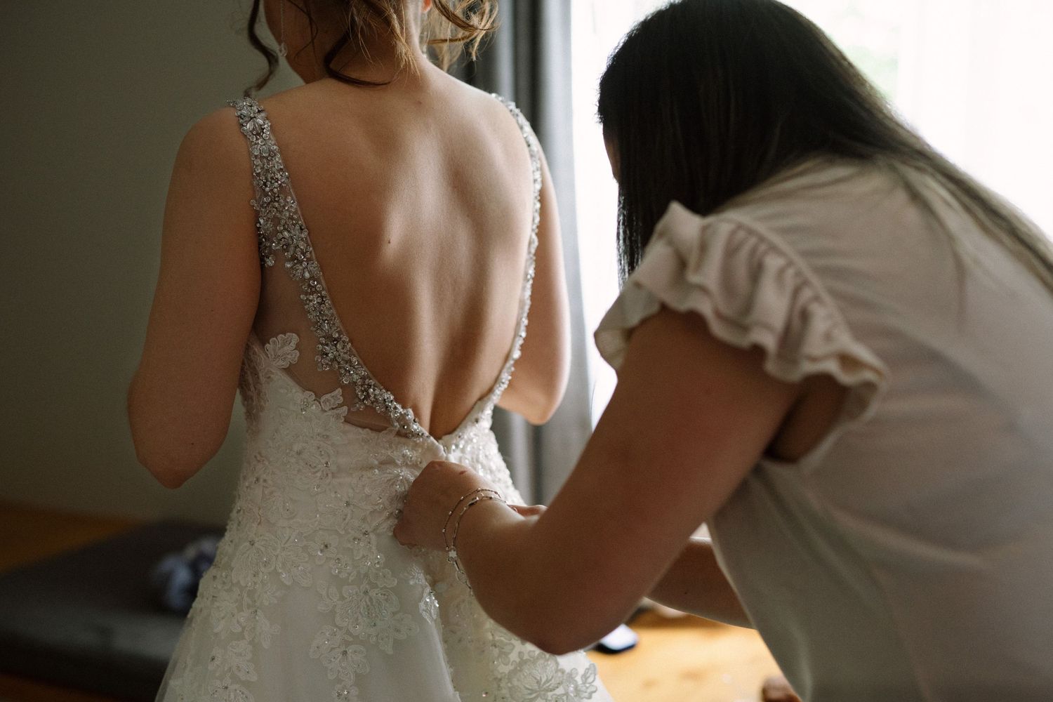 Detail shot of wedding dress being buttoned up with intricate beaded back.