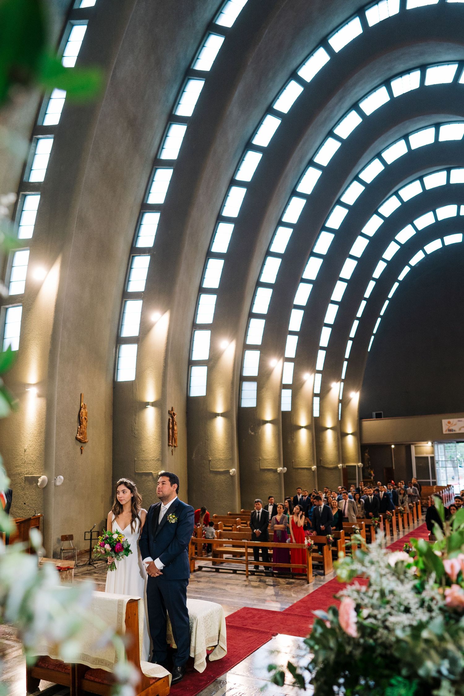 Modern church interior with curved ceiling windows illuminating a wedding ceremony.