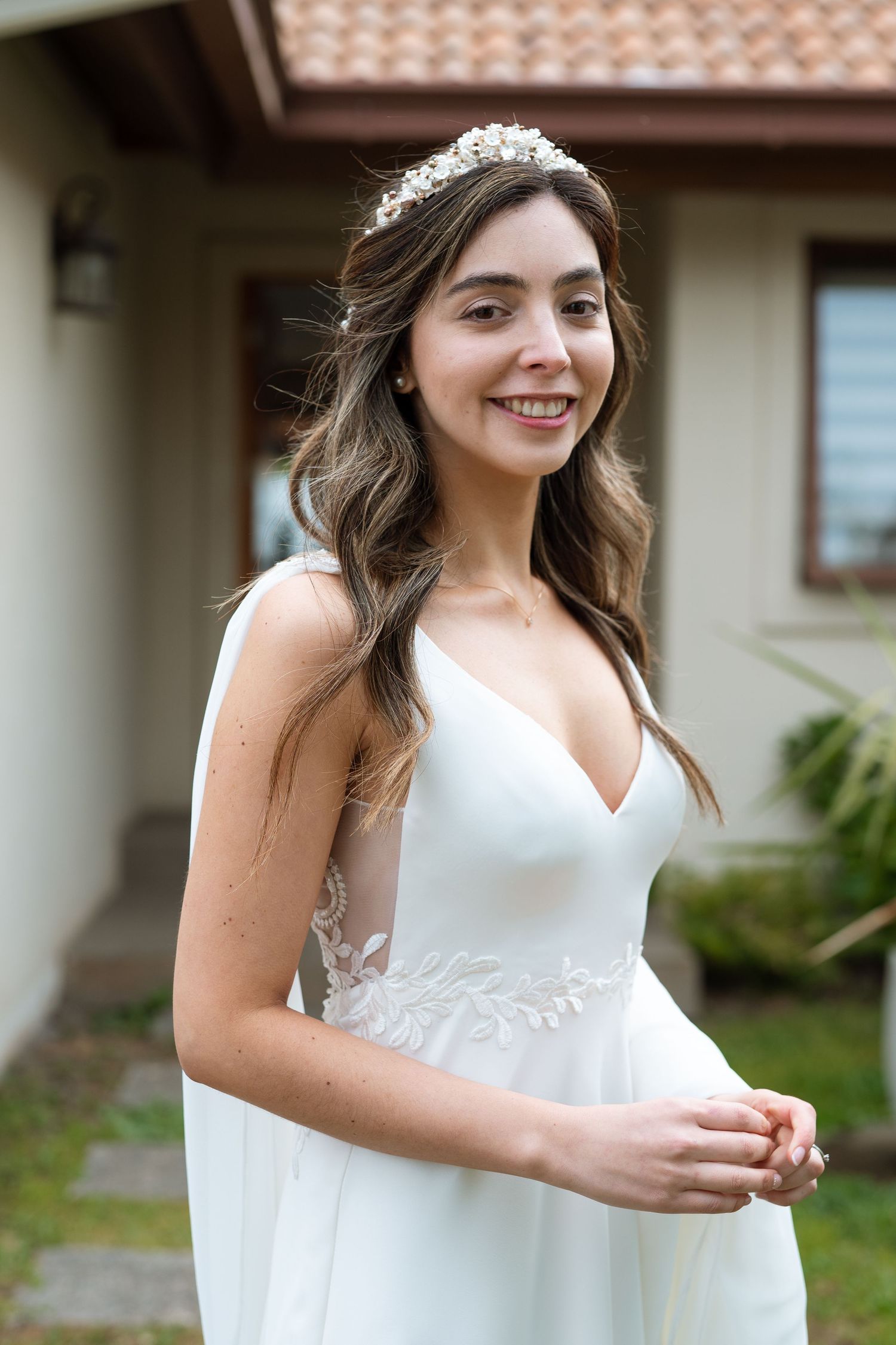 A bride wearing a delicate tiara and white wedding dress poses outdoors on her wedding day.