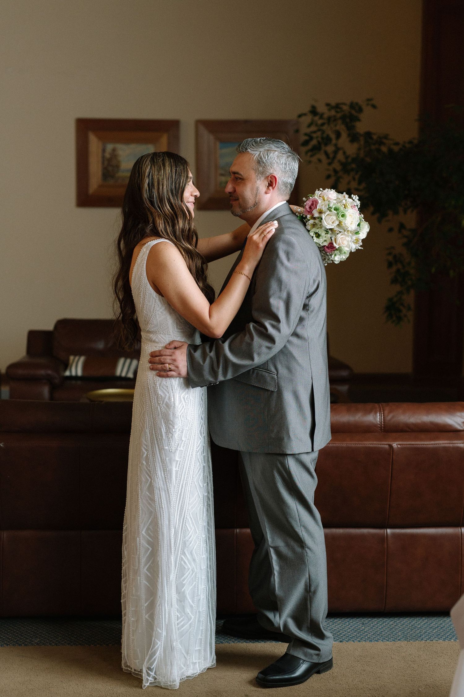A tender embrace between newlyweds against a brown leather couch backdrop.