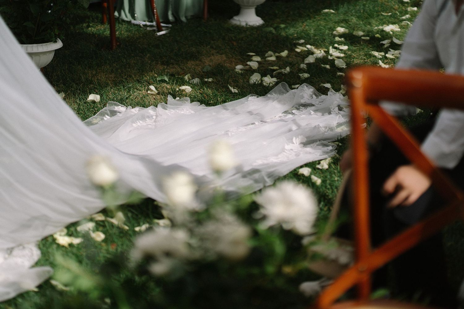 Wedding veil train spread across green grass with white flower petals at an outdoor ceremony.