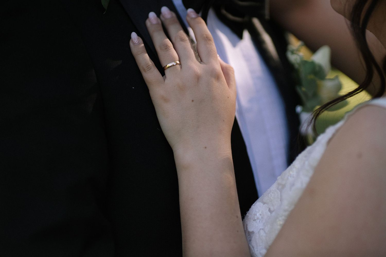 Close-up of a wedding ring displayed on a hand against formal attire.