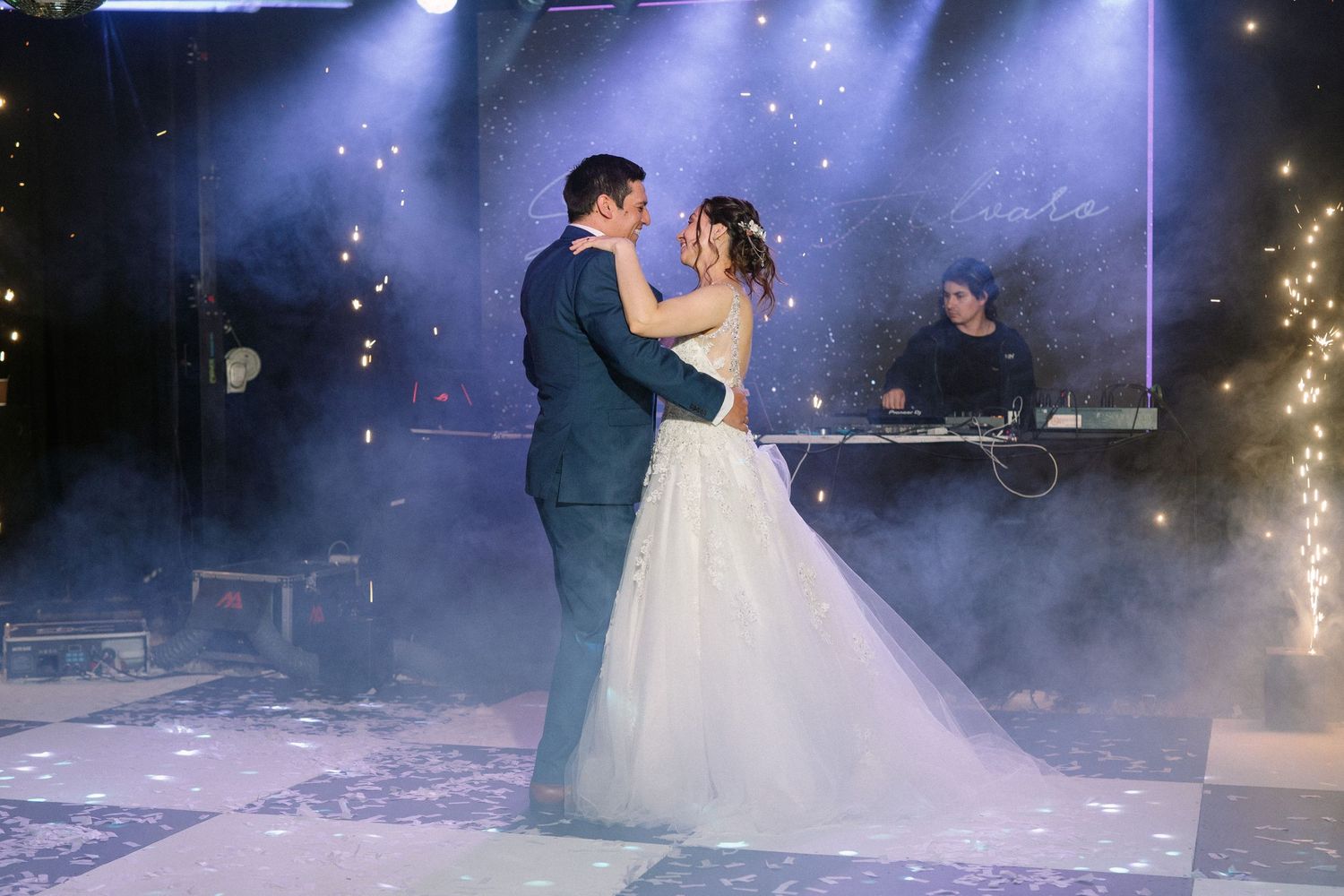 A beautiful wedding dance moment captured with atmospheric fog and sparkling lights in the background.