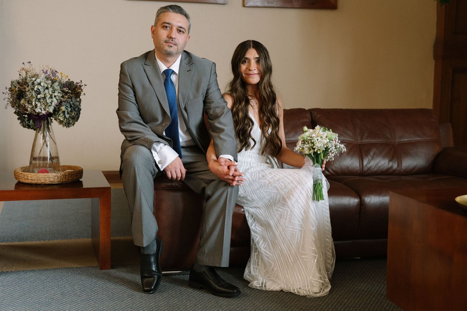Couple sitting together on leather couch during wedding photoshoot.