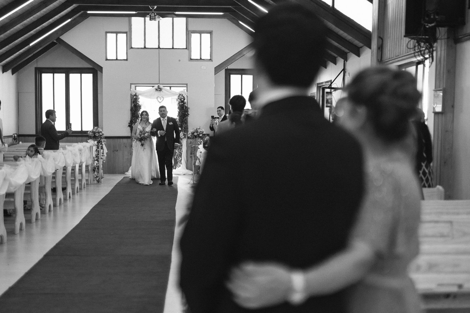 A black and white photo captures a wedding ceremony processional in a church with high ceilings.