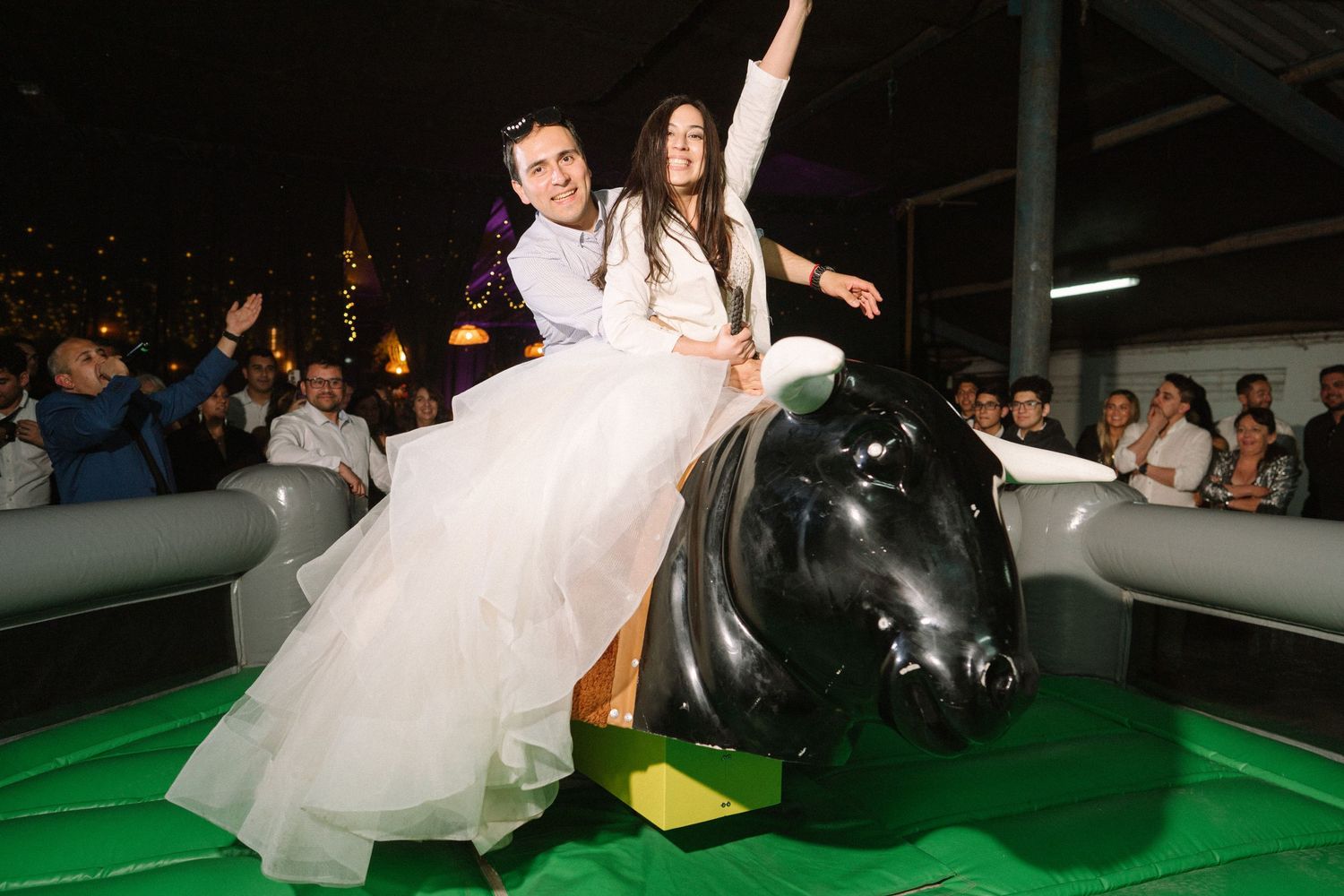 A couple rides a mechanical bull at their wedding reception.