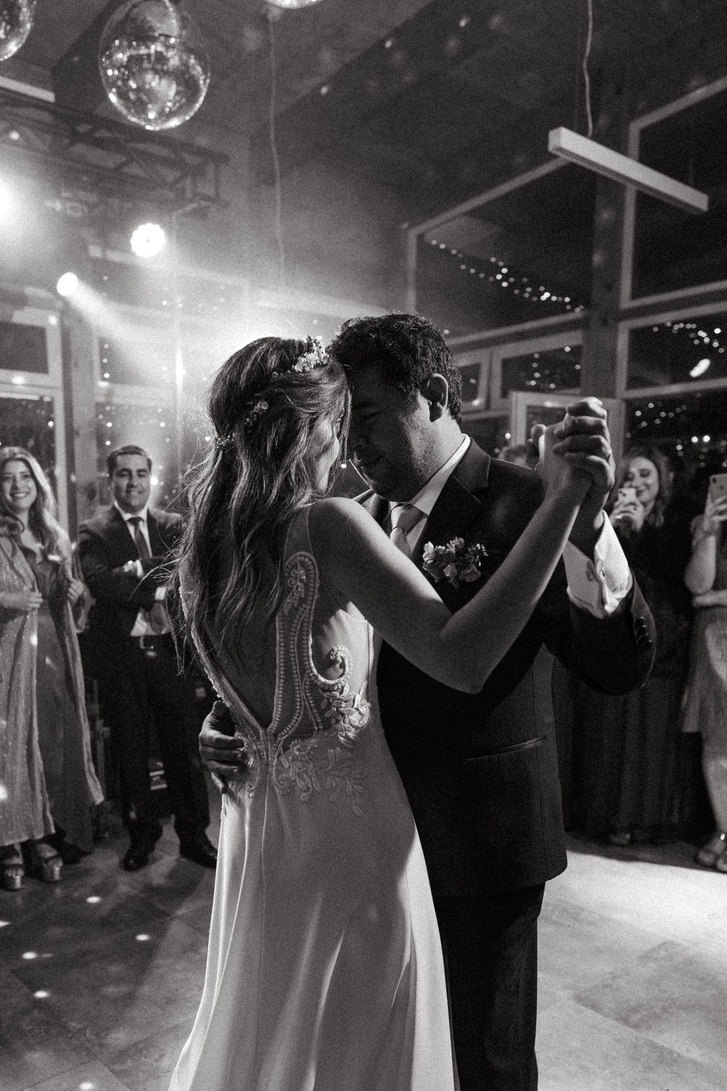 A romantic black and white photo of a couple dancing under disco balls and spotlights.