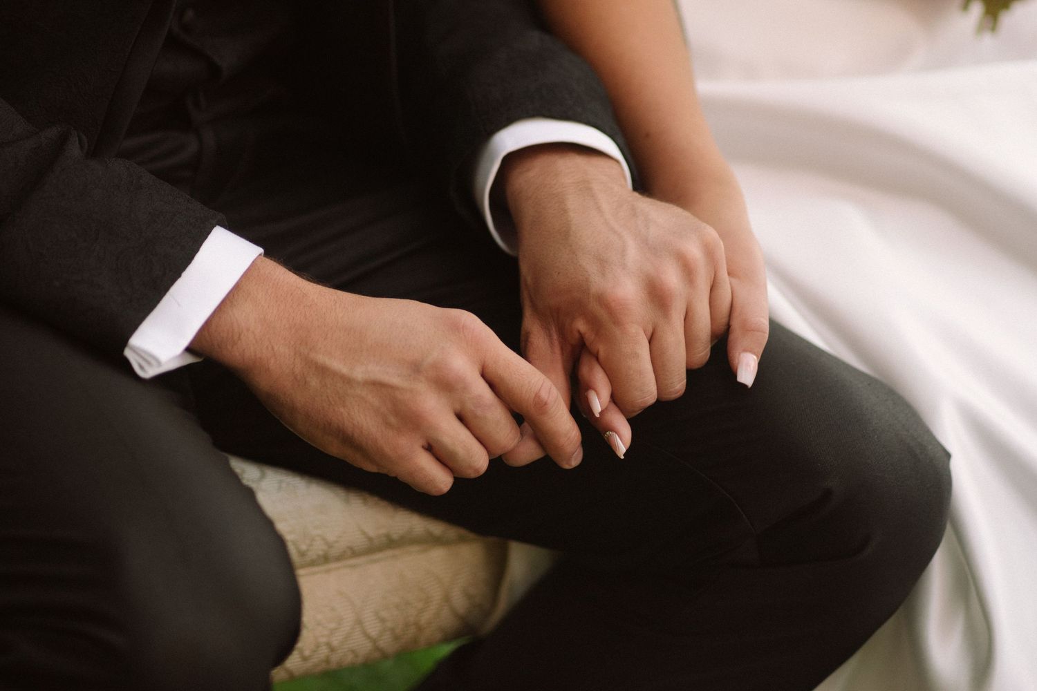 Close-up of hands resting on formal attire during outdoor wedding ceremony.