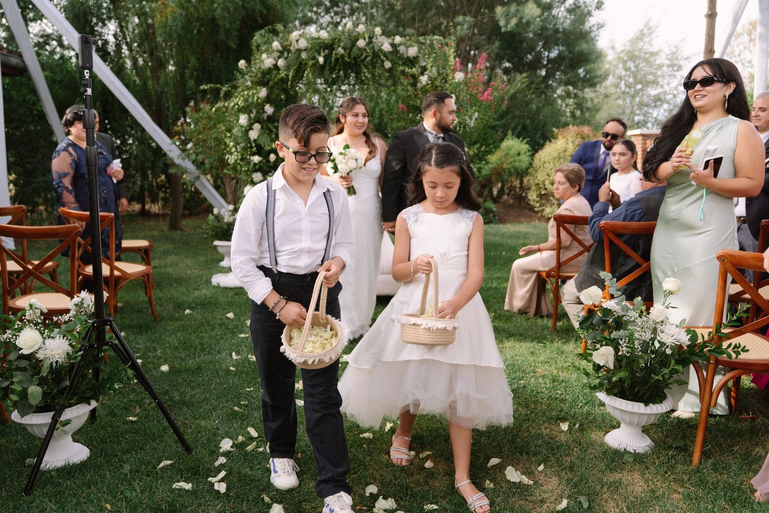 Young flower girl and ring bearer walking down outdoor wedding ceremony aisle with baskets.
