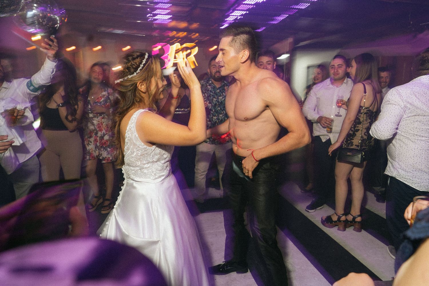 A bride dances with a shirtless guest during wedding party celebrations.