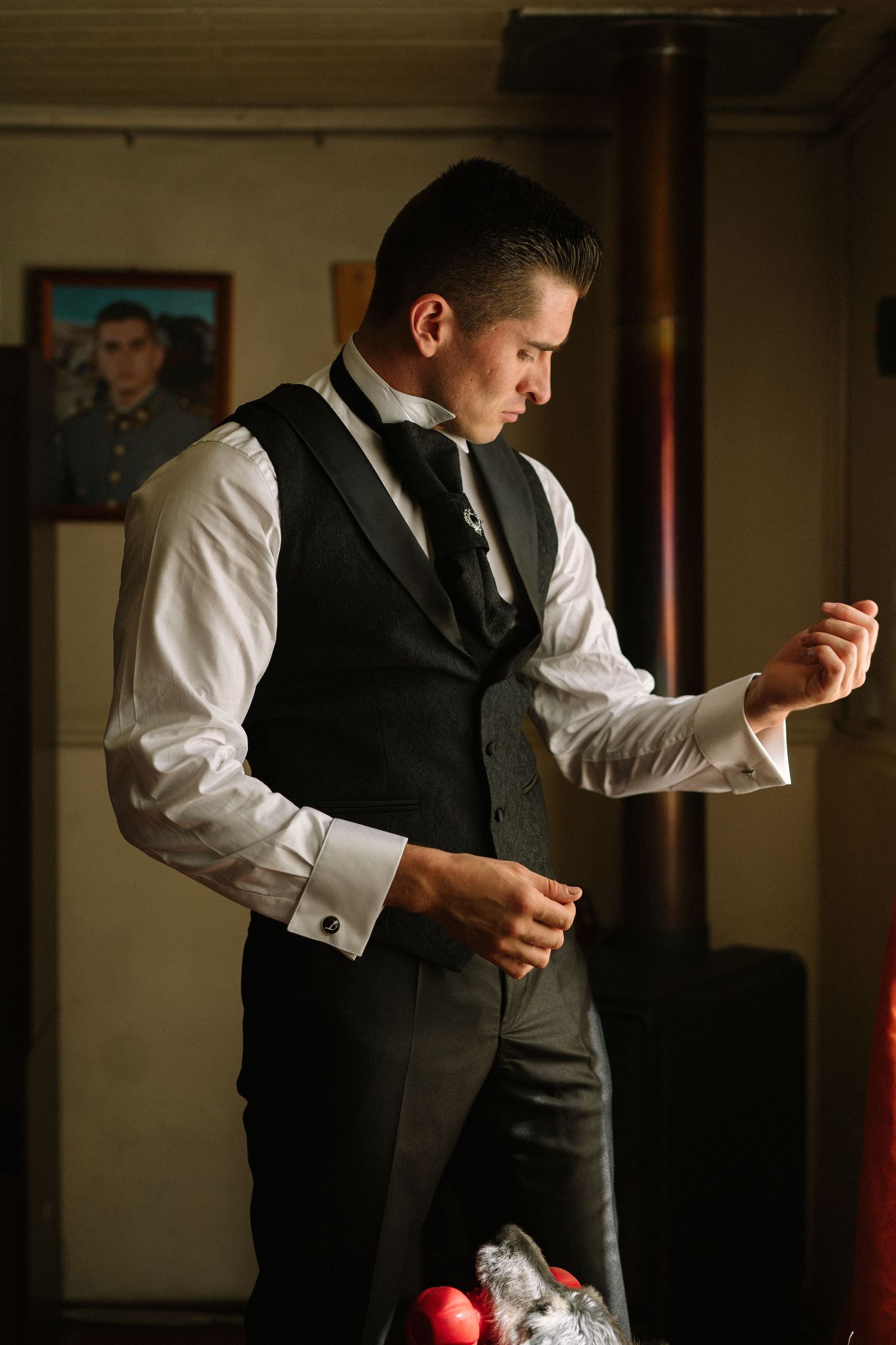 Person in formal vest and white shirt adjusting cuffs in indoor setting.