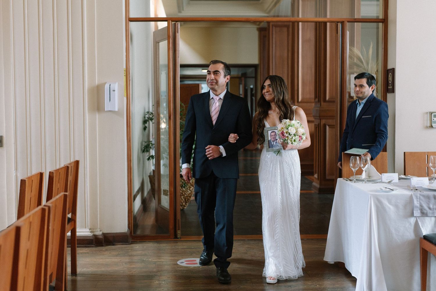 A formal ceremony procession walks through an elegant hallway with table settings.
