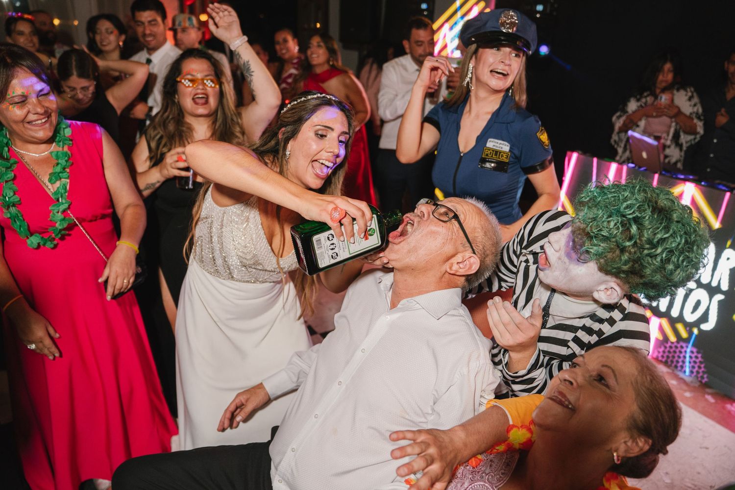 Wedding reception guests dancing and celebrating on a dark dance floor with colorful lighting.