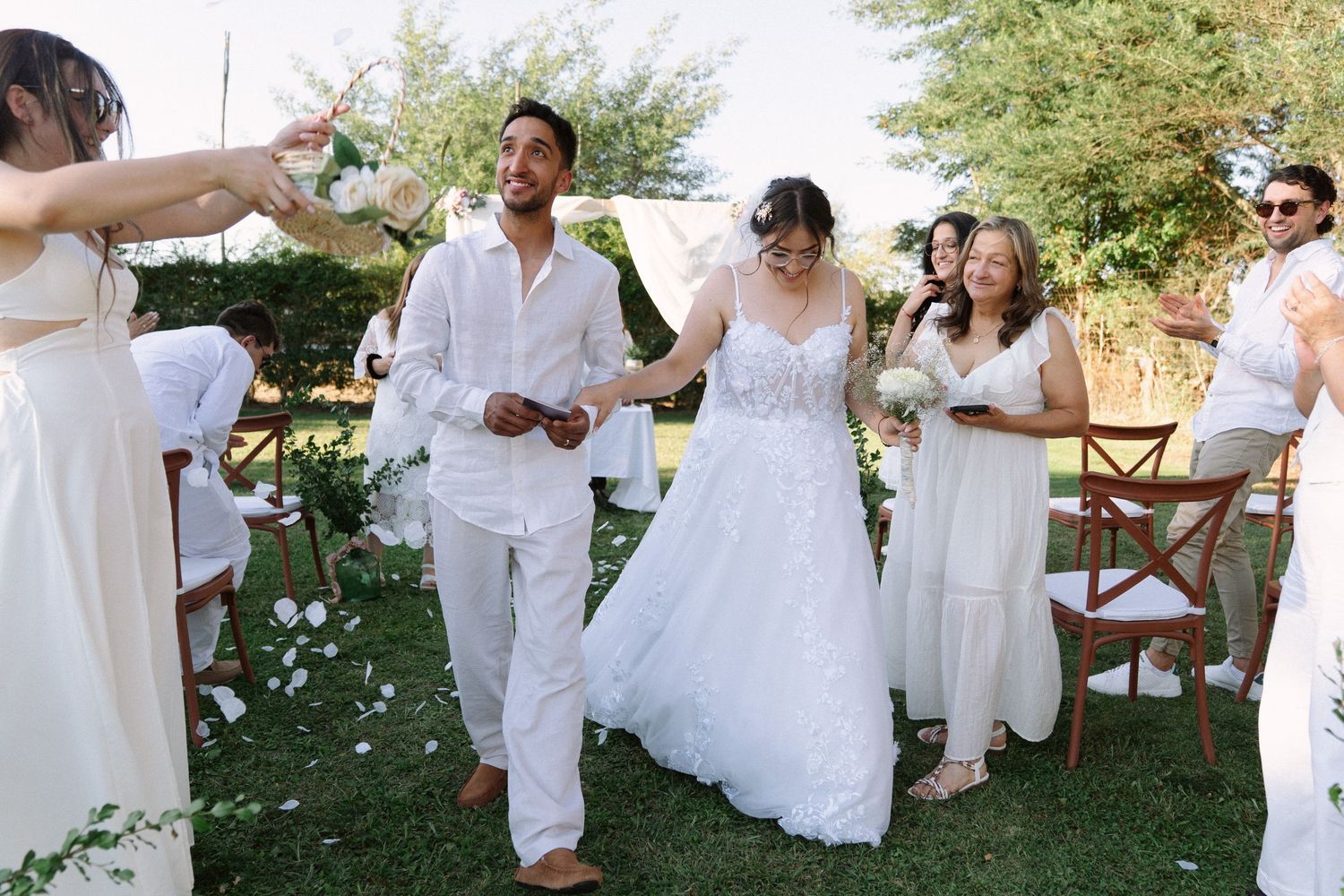 Newlywed couple walks joyfully down the aisle as guests celebrate with confetti at outdoor garden wedding.