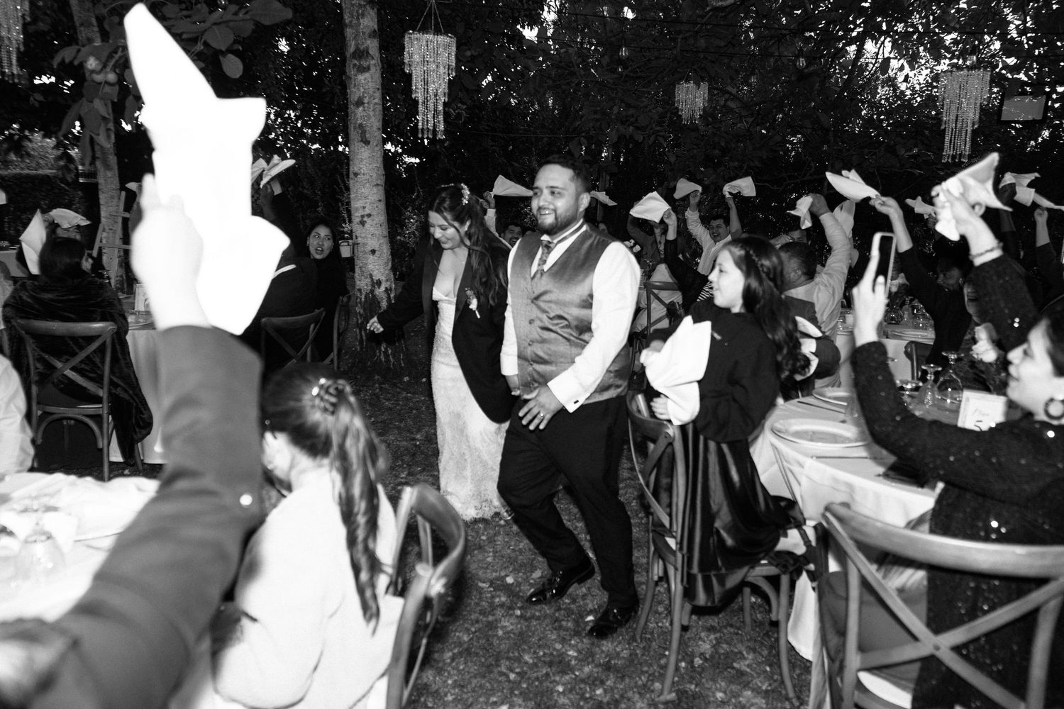 Lively black and white wedding reception dance with guests waving napkins around couple.