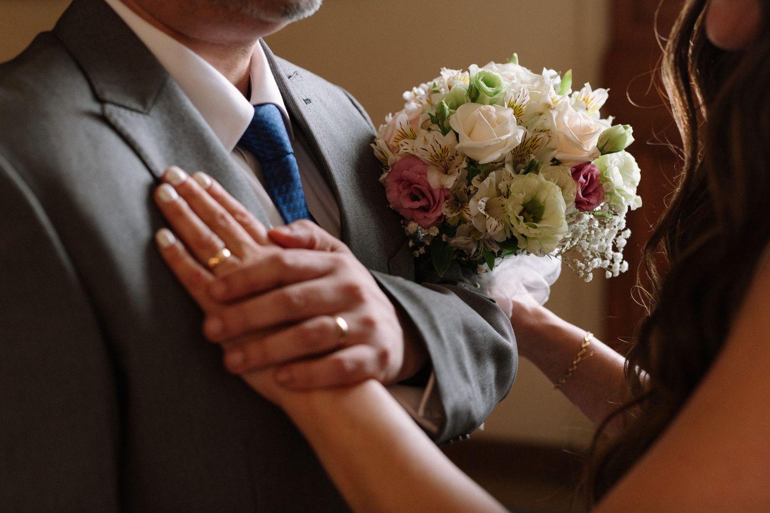 Wedding details showing hands, rings, and a pink and white bridal bouquet.