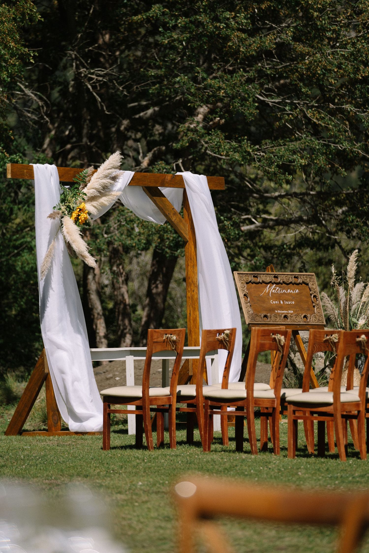 An outdoor wedding ceremony setup with wooden chairs and white fabric archway in a garden setting.