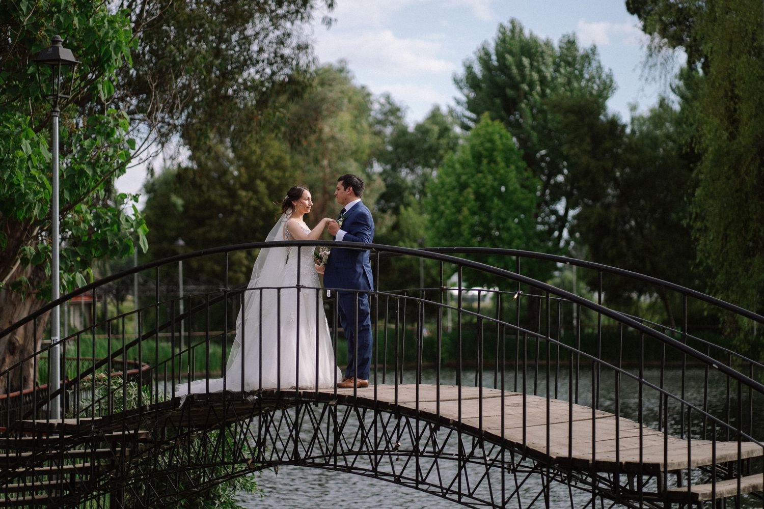 Newlyweds standing together on an ornate bridge in a garden setting.