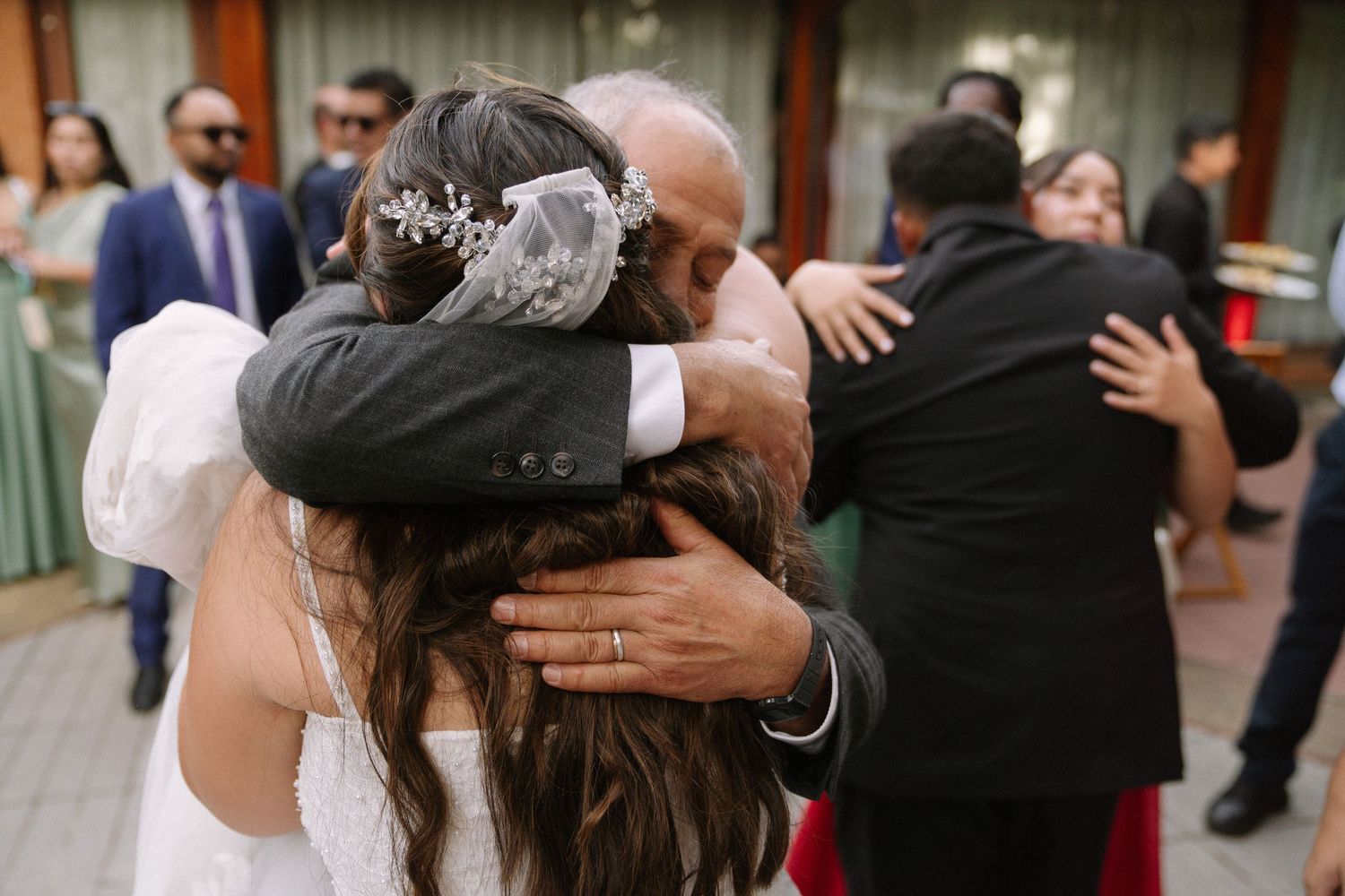 A bride in a white gown shares a heartfelt embrace with family members at her wedding reception.
