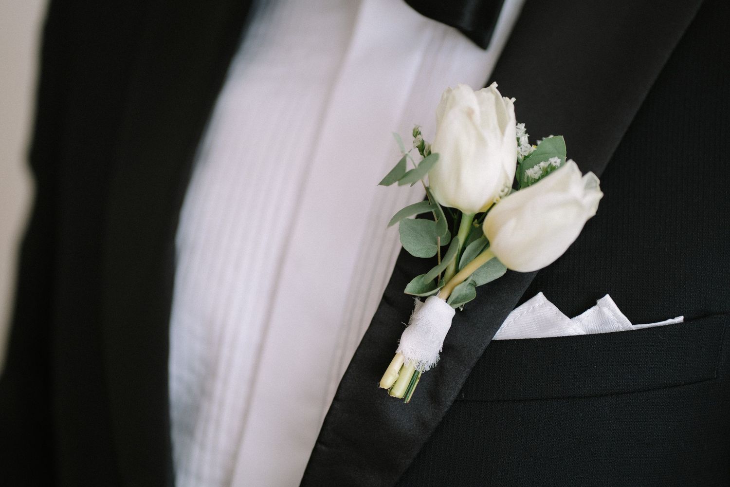 White rose boutonniere with eucalyptus leaves pinned to black suit jacket.