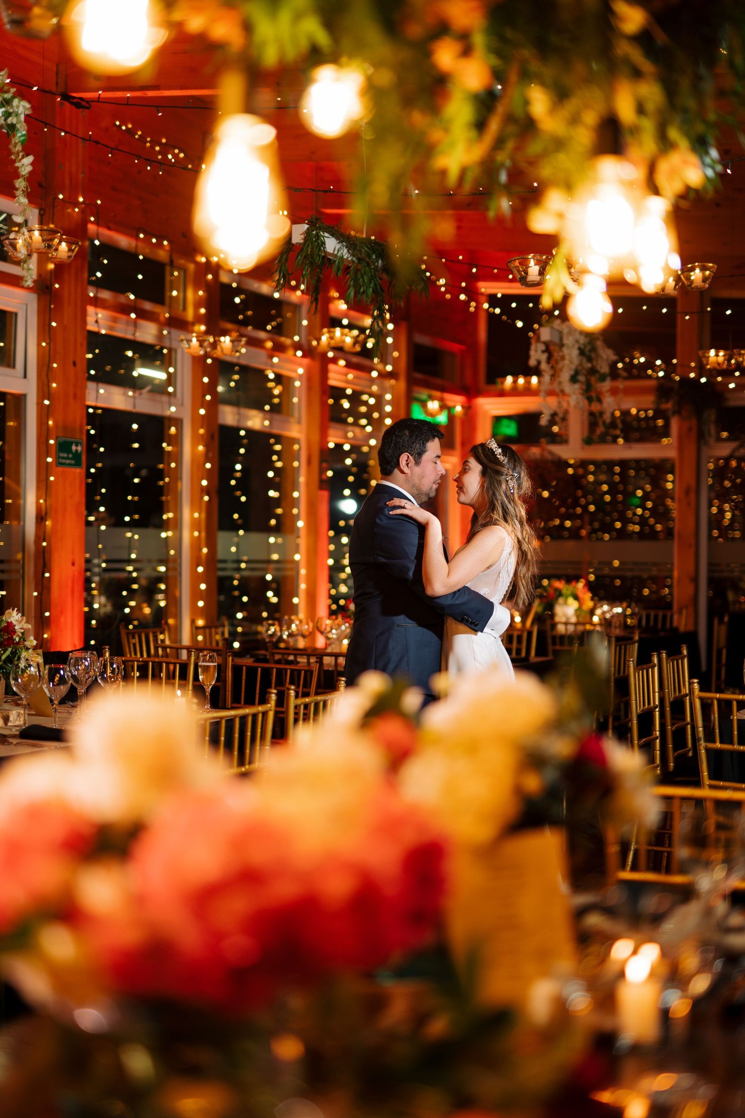 Wedding reception venue decorated with hanging lights and floral arrangements creating romantic ambiance.