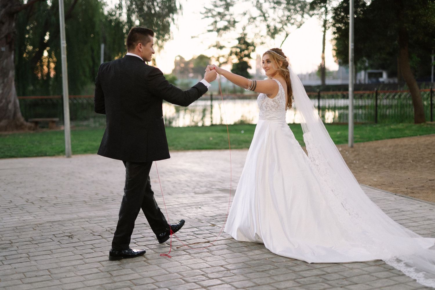 A joyful wedding couple dances together on a paved outdoor path.