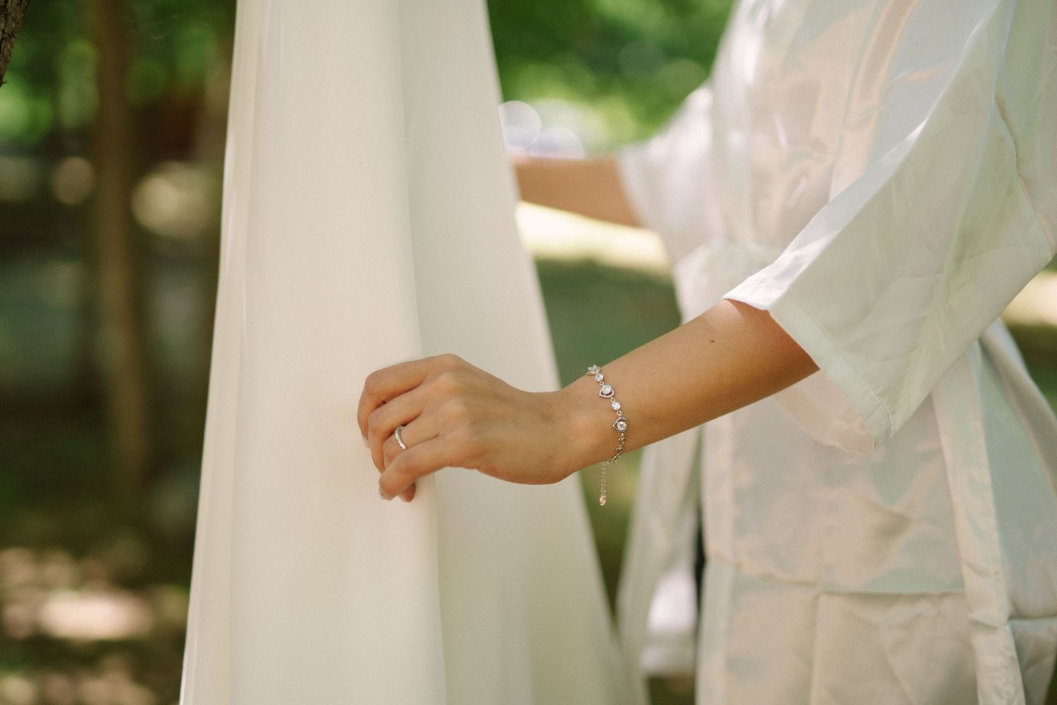 Close-up detail of a bracelet on a person's wrist near white wedding fabric.