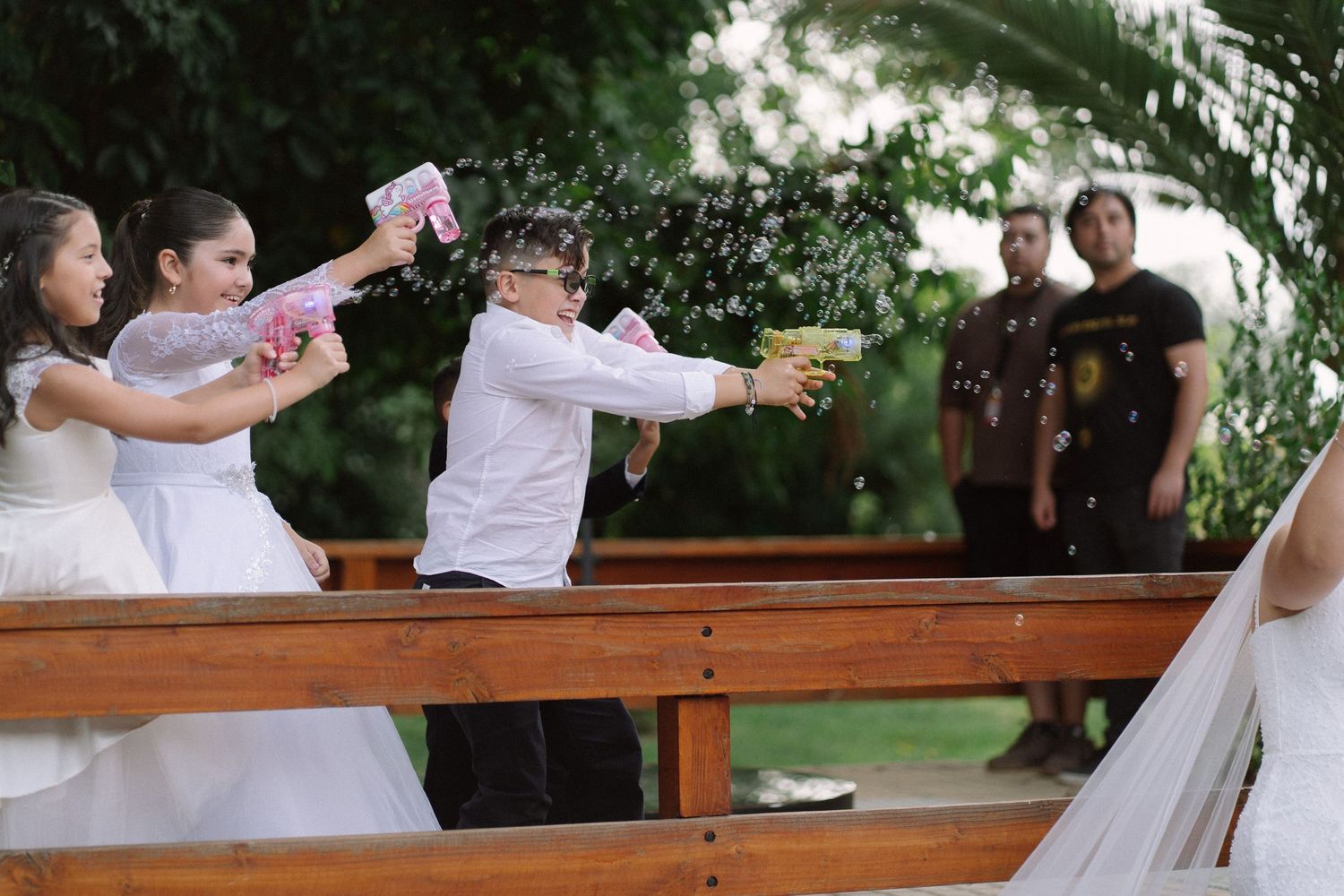 Children playfully shoot water guns at wedding guests during a fun outdoor ceremony celebration.