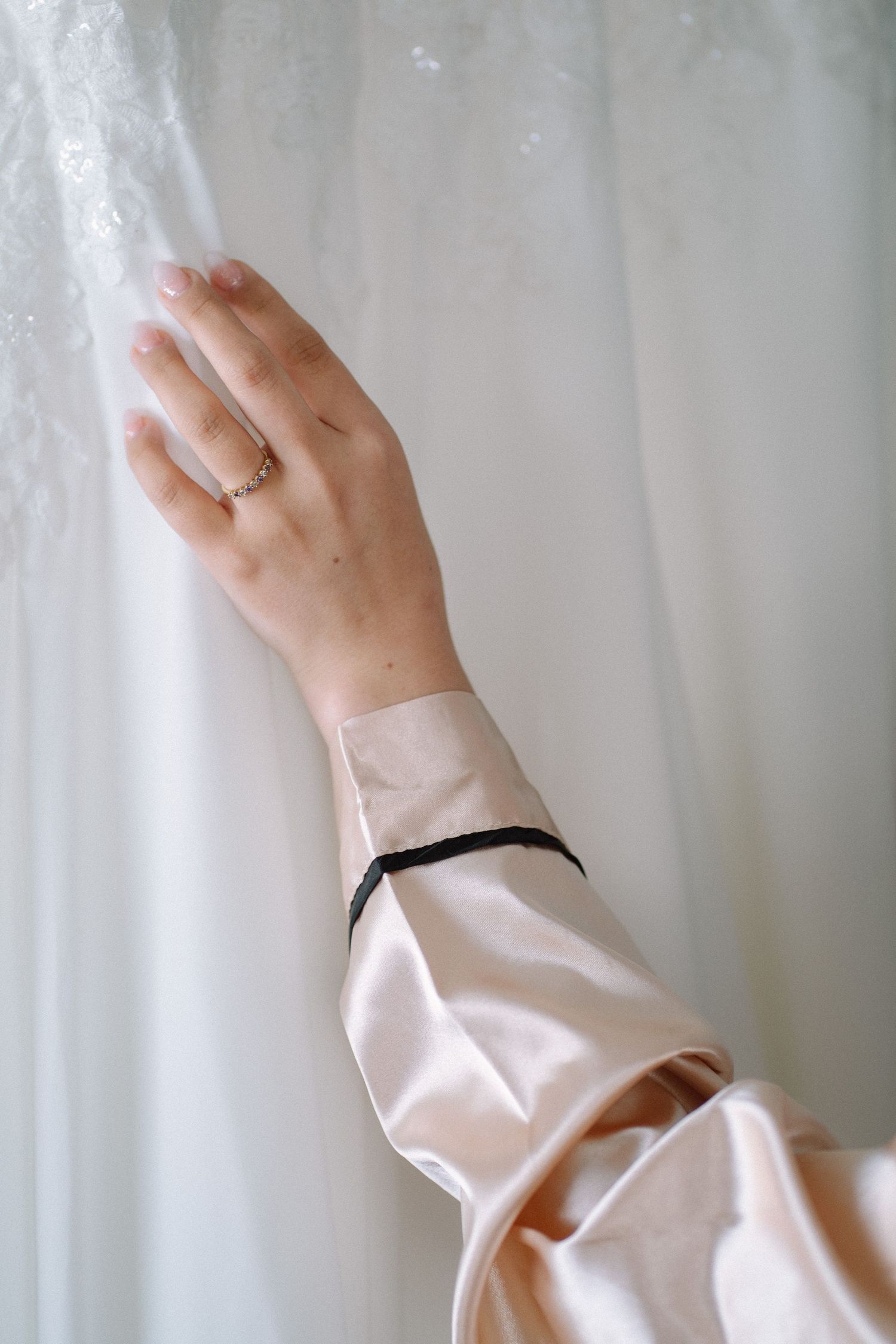 Hand wearing engagement ring reaches to touch white wedding dress fabric.