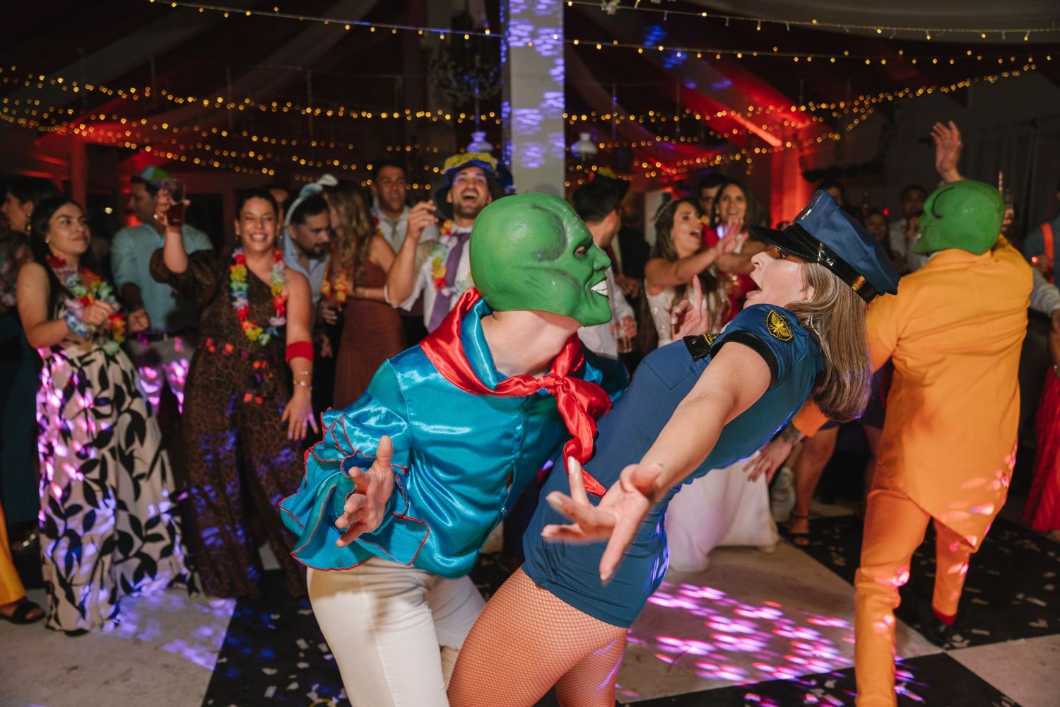 Colorfully dressed wedding guests dancing under string lights at a reception party.