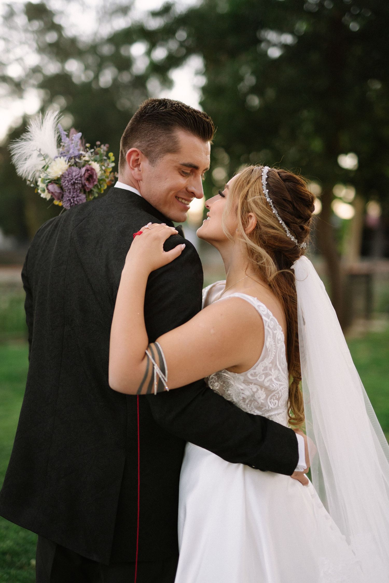 A romantic wedding embrace captured in a park setting with floral bouquet details.