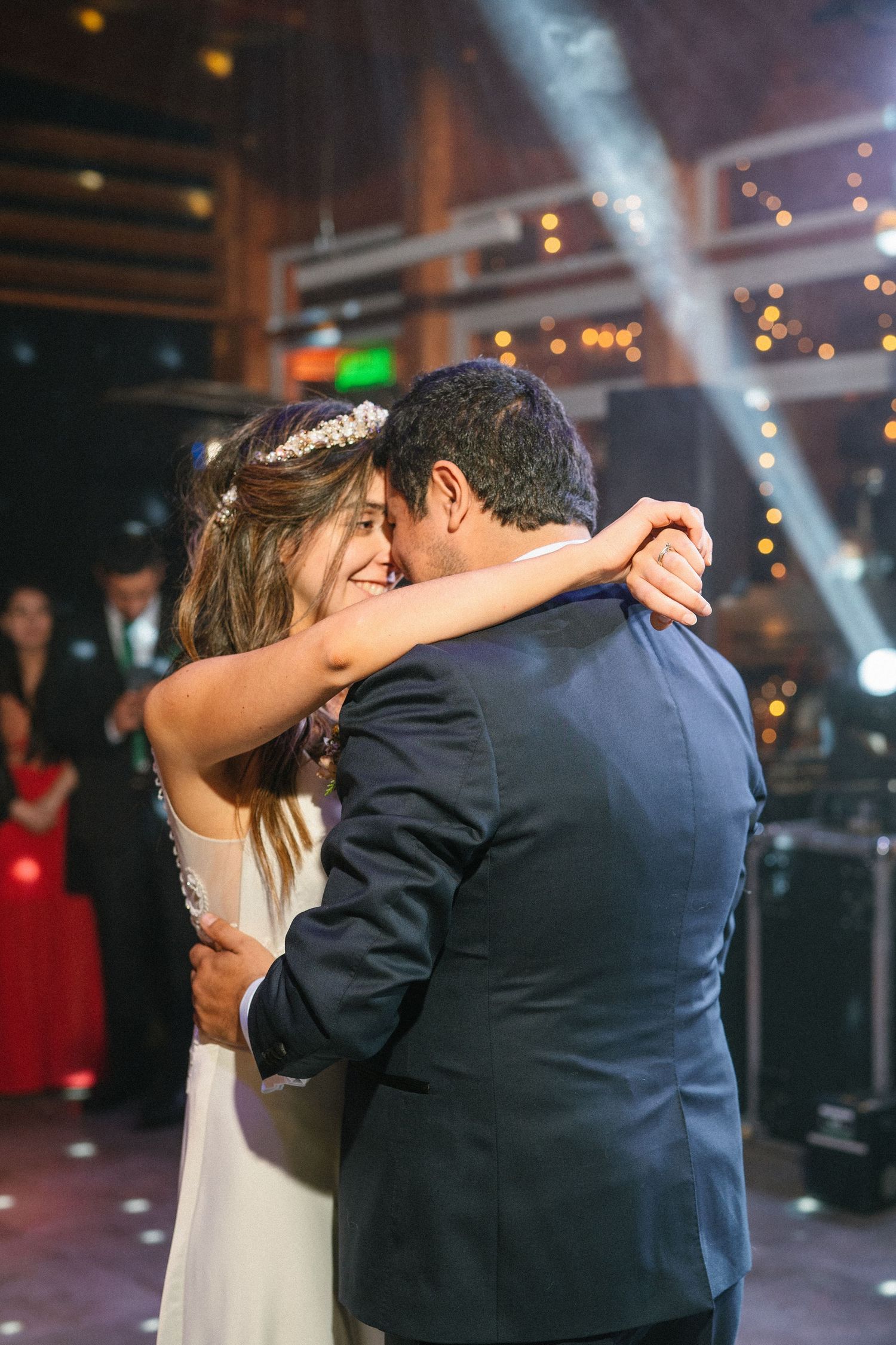 A couple embraces closely during their wedding dance under twinkling lights.