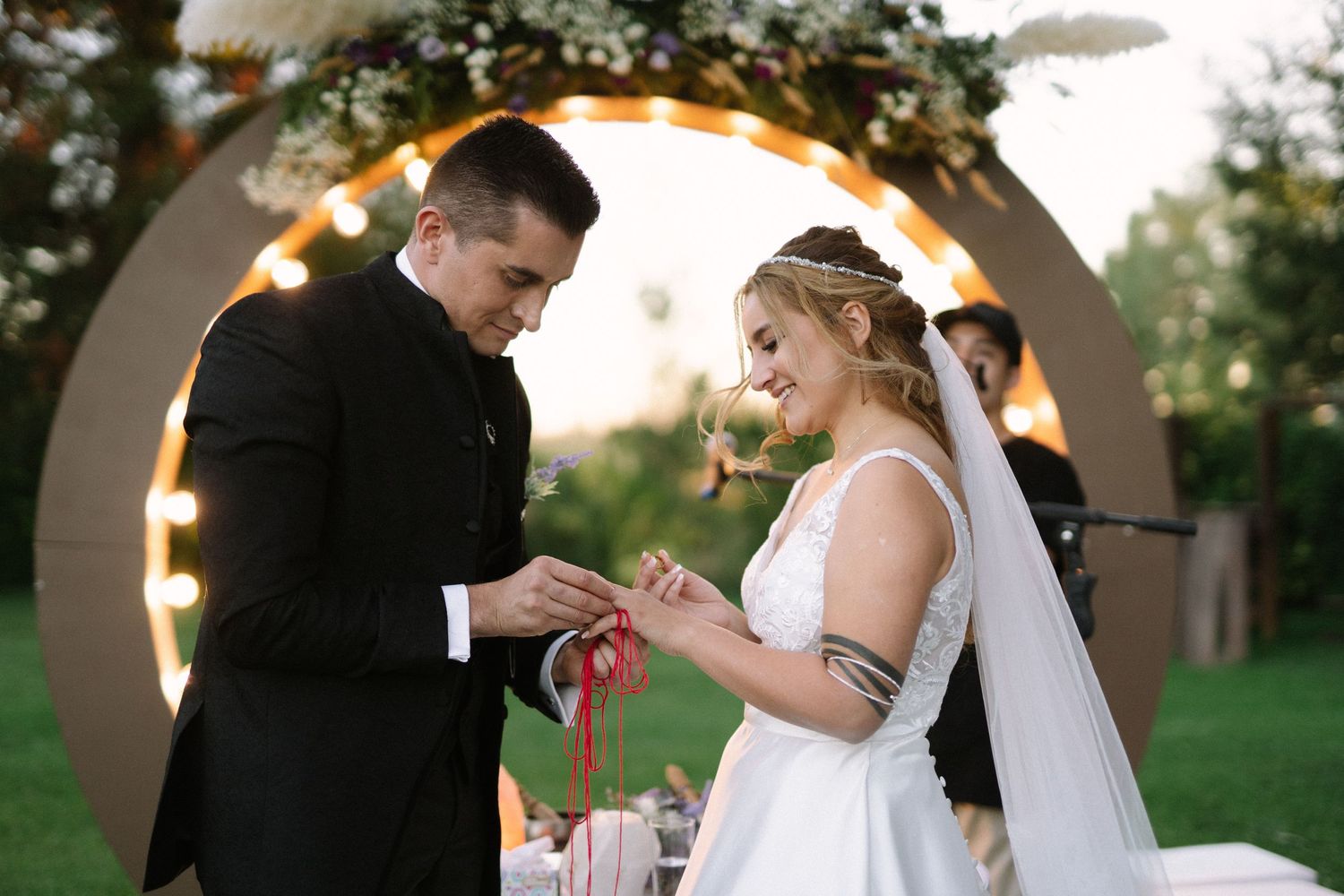 Couple participates in a ring exchange ceremony under an illuminated round arch.