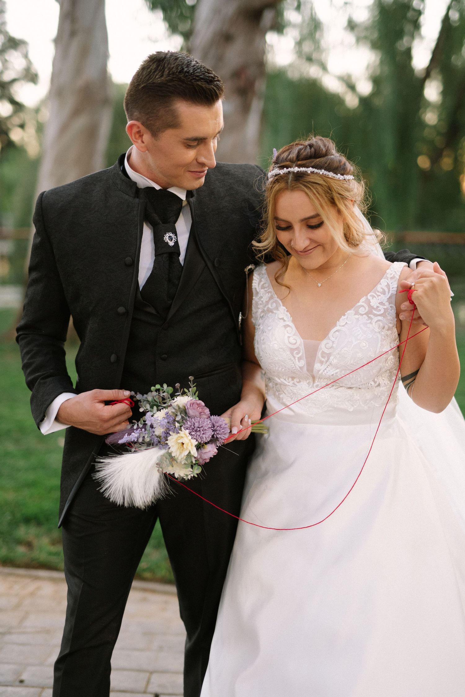 An elegant wedding portrait featuring formal attire and delicate floral details in a park setting.
