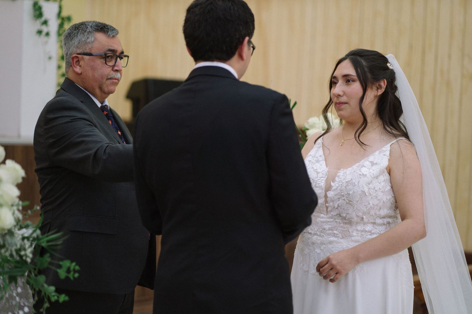 A wedding ceremony takes place at the altar of a traditional church with decorative floral arrangements.