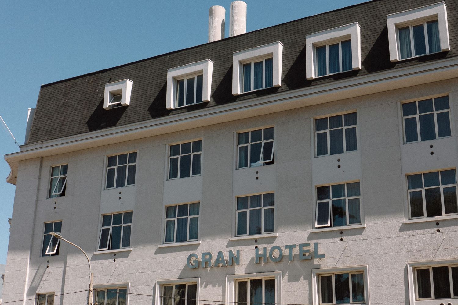 Exterior view of a multi-story hotel building with white facade and mansard roof against blue sky.