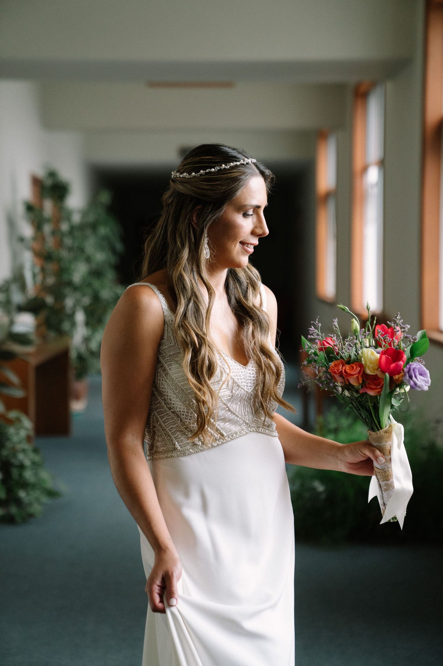 A bridal bouquet of red and purple flowers with white ribbon against an interior hallway background.