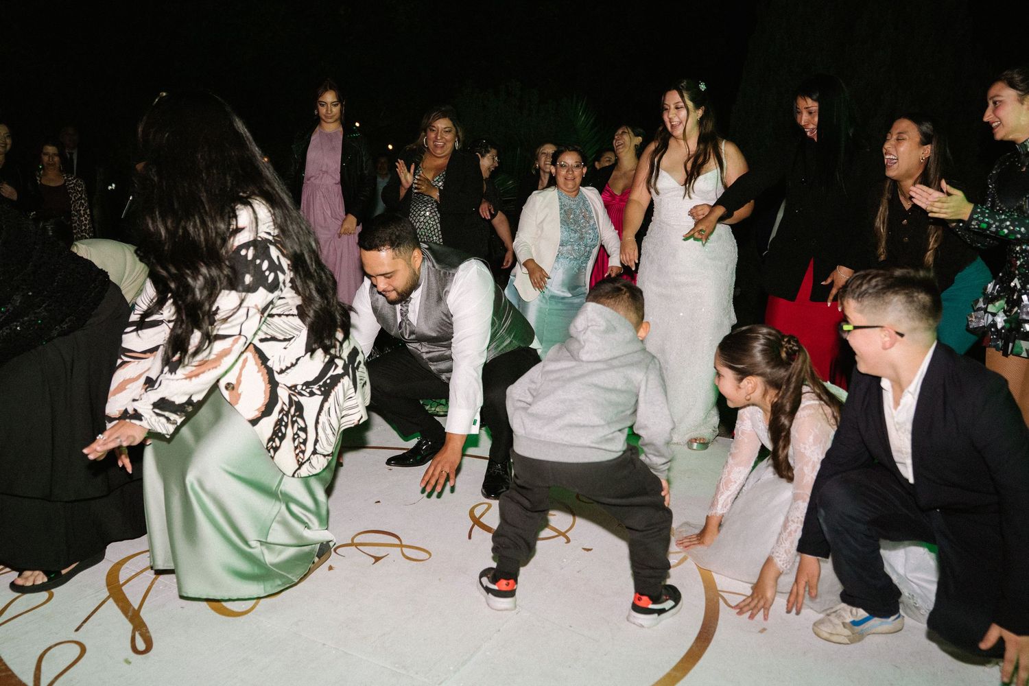 Wedding guests dance and celebrate energetically on a white dance floor during a lively reception party.